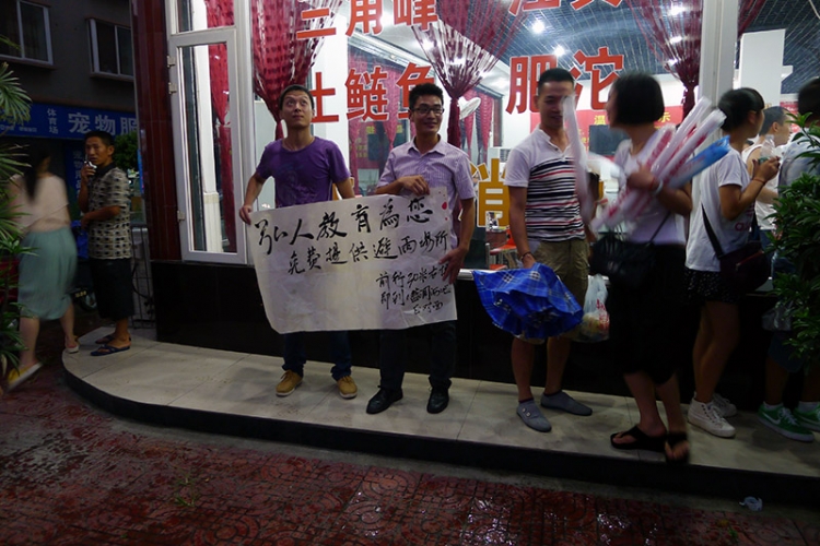 暴雨袭来街边两位帅哥扯起墨迹未干的横幅“弘人教育免费提供避雨场所”左边的帅哥望着.jpg