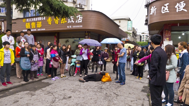 天在下雨，两位美女为倒在地上的 老人撑伞